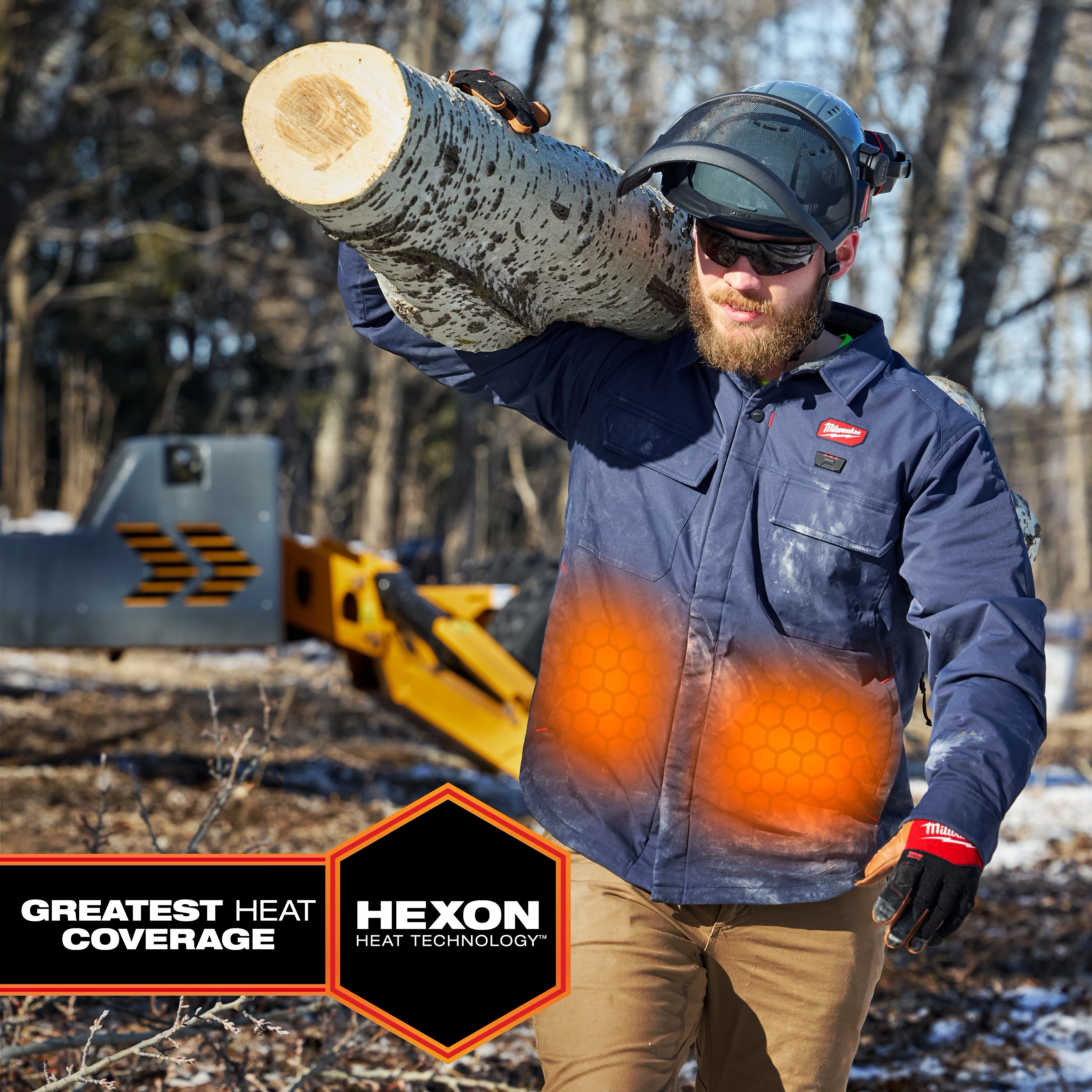 Worker carrying a log wears M12 Shirt Jacket - Navy L with glowing orange heat zones and HEXON HEAT TECHNOLOGY badge.