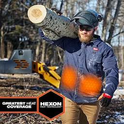 Worker carrying a log wears M12 Shirt Jacket - Navy L with glowing orange heat zones and HEXON HEAT TECHNOLOGY badge.