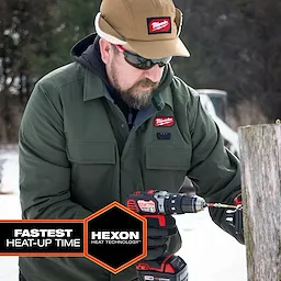 Person using a power drill outdoors while wearing an M12 Shirt Jacket - Green L in a snowy setting.