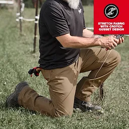 A man is kneeling outdoors, wearing tan Work Pants and a black shirt. The pants feature stretch fabric with a crotch gusset design, highlighted in a red upper right corner of the image. The person is holding a tool and has multiple items attached to their belt.