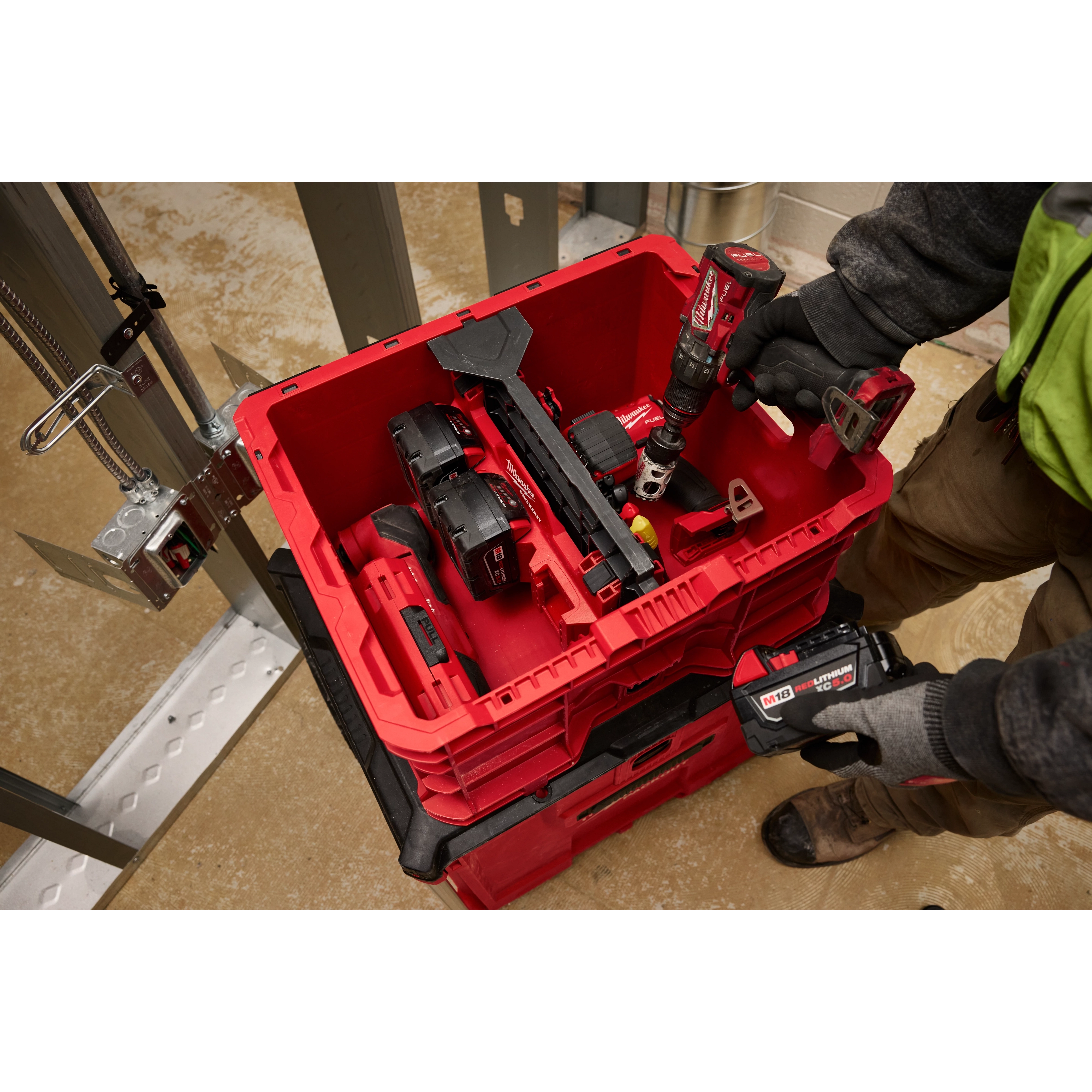 Worker placing a divider into a PACKOUT Crate filled with various power tools and accessories in a workshop setting.