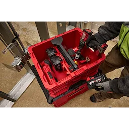 Worker placing a divider into a PACKOUT Crate filled with various power tools and accessories in a workshop setting.