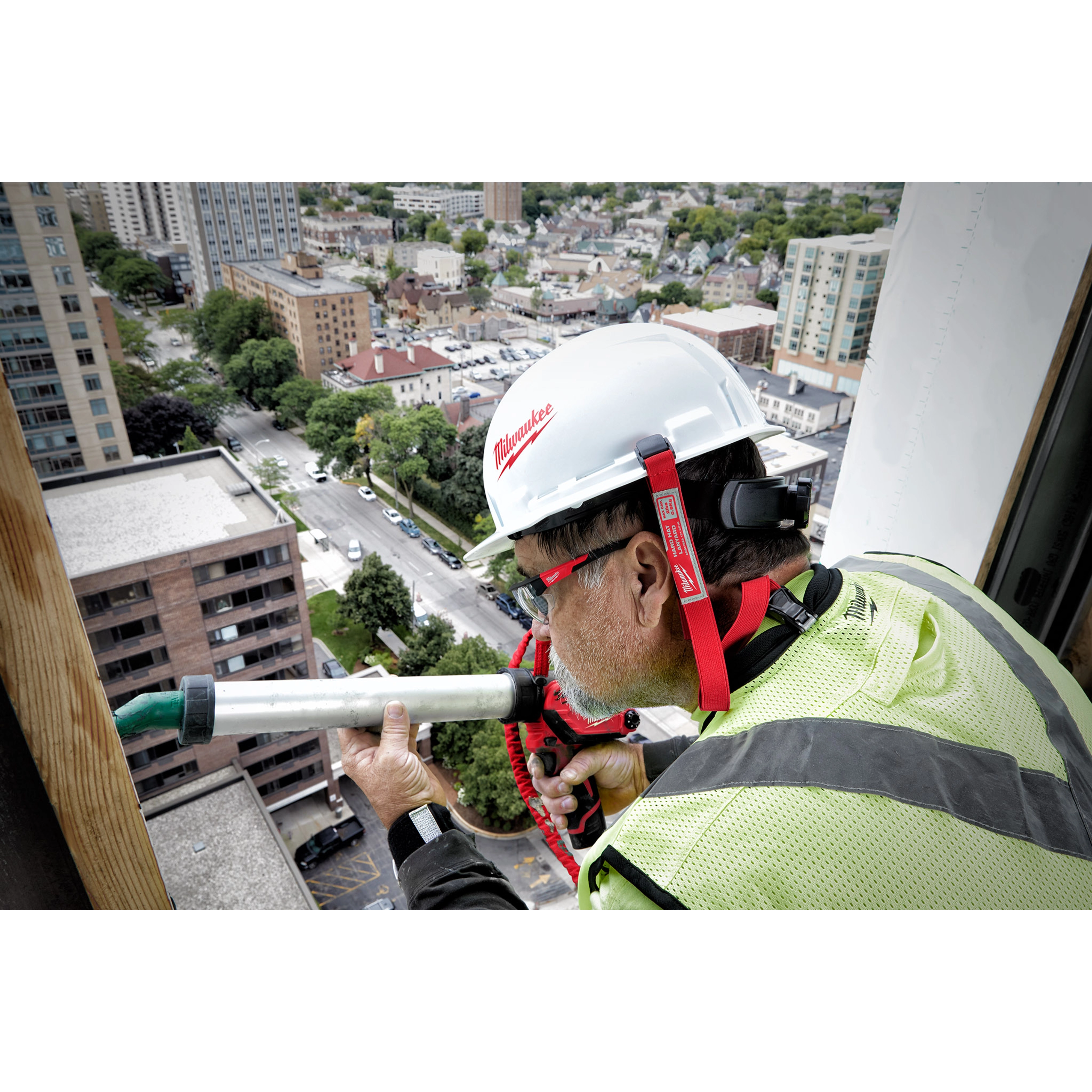 Worker on a high-rise building wears a white hard hat secured with a red Hard Hat Lanyard with Clip and holds a pipe.