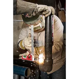 Welder using a 12" Magnetic Combination Square to measure a metal pipe with a spirit level attached. Welding sparks visible.