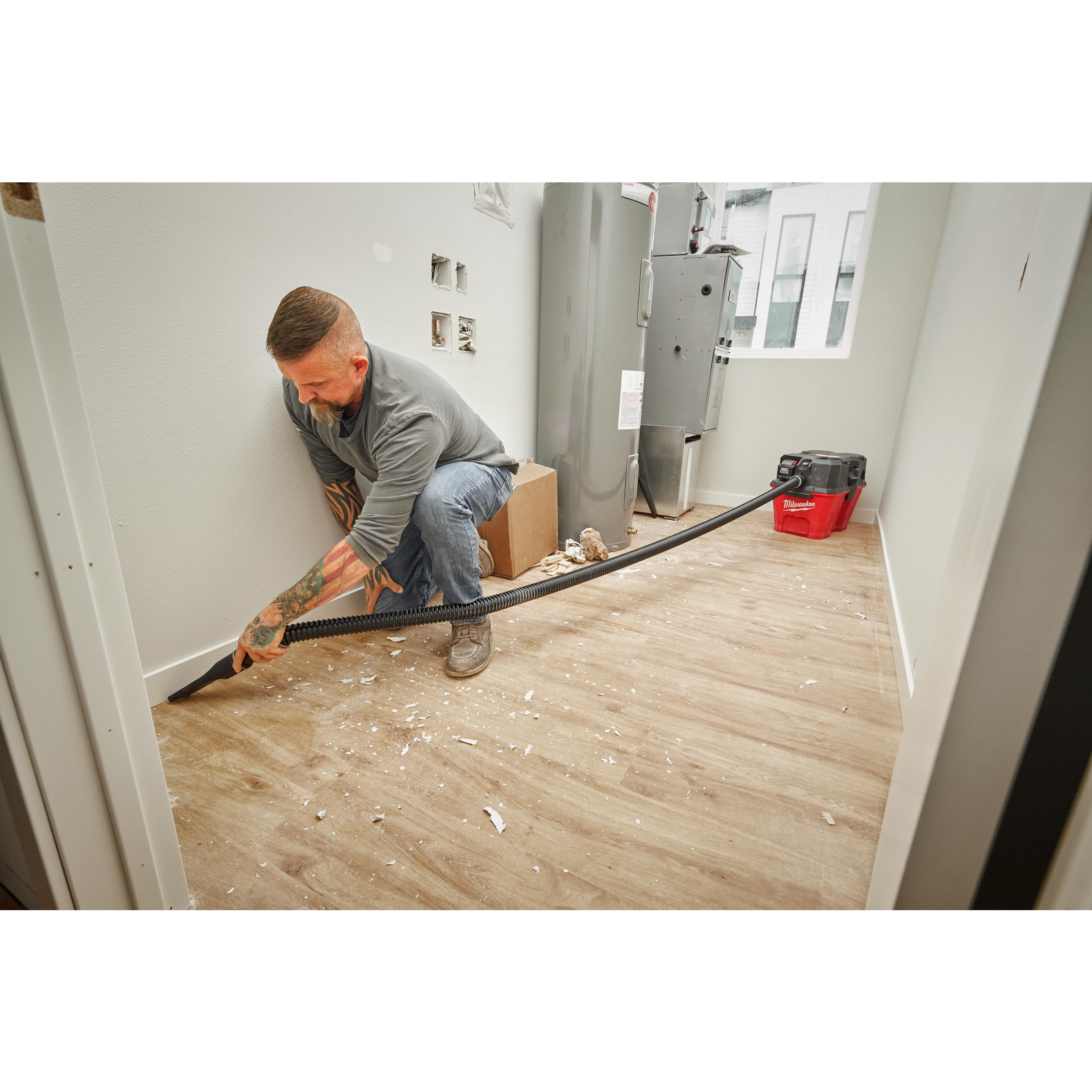 A person uses a shop vacuum with a 1-7/8” x 32” to 102” expandable hose to clean up construction debris from a floor.