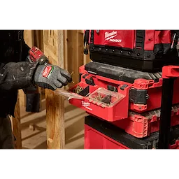 A person wearing work gloves uses the PACKOUT Tool Box 2-Bin Attachment to organize screws, shown attached to a red tool storage system.