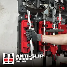 Gloved hand placing a tool in the PACKOUT Long Handle Tool Holder, featuring anti-slip rubber grips, mounted on a black and red wall storage system.