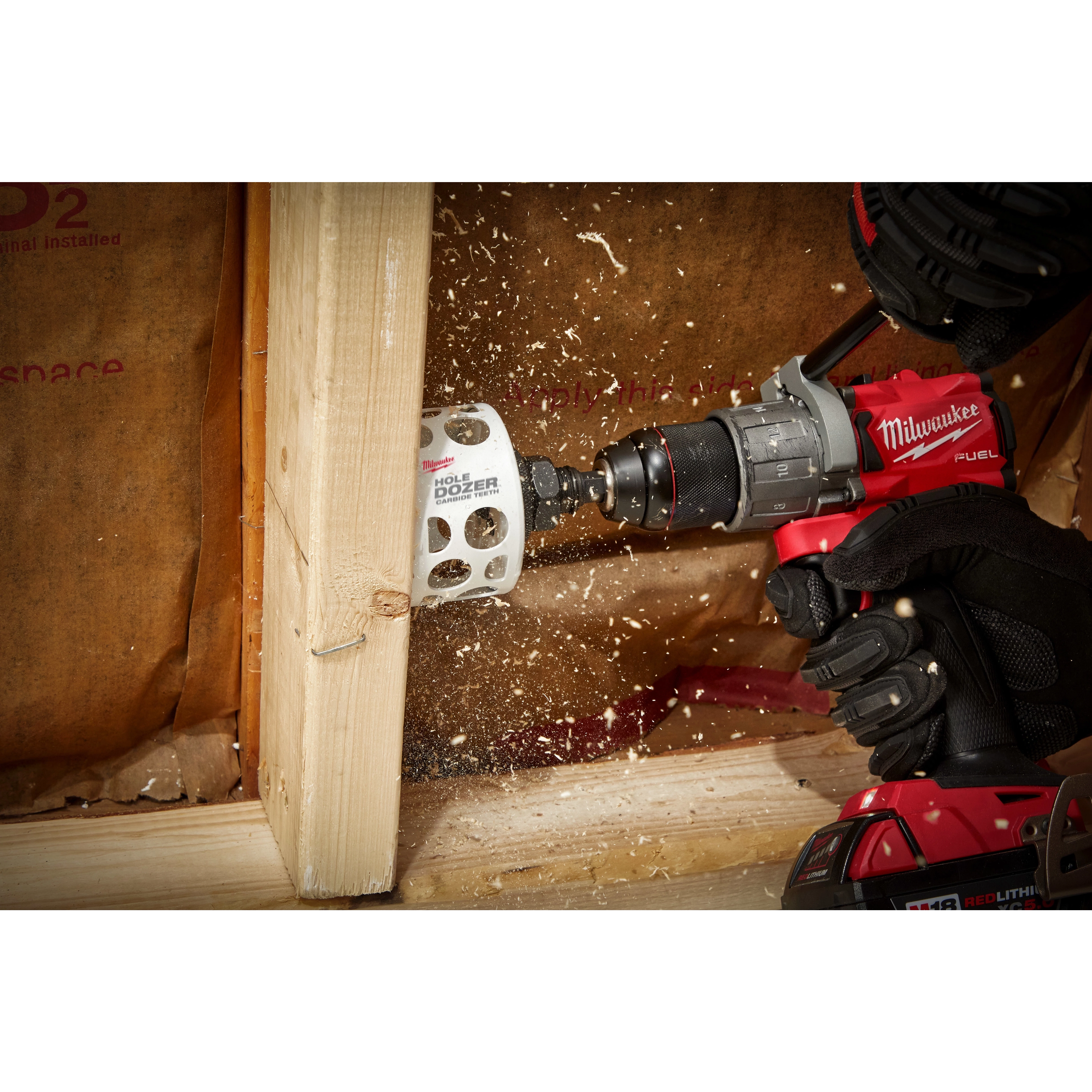 A 3-inch Hole Dozer with Carbide Teeth Hole Saw is mounted on a power drill, cutting through a wooden beam.