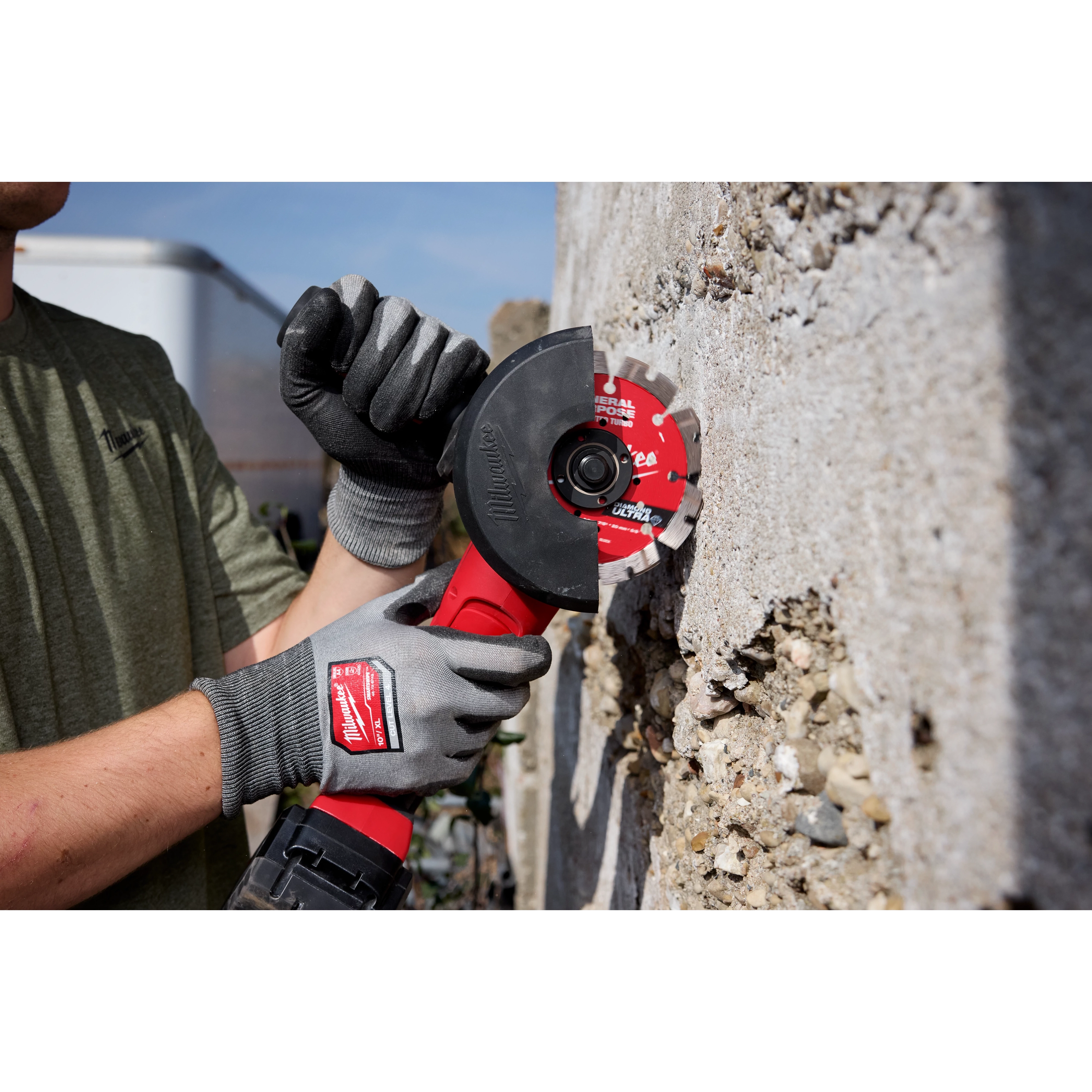 A person wearing gloves is using a 4" DIAMOND ULTRA™ Segmented Turbo Blade attached to an angle grinder to cut through a concrete surface.