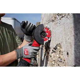 A person wearing gloves is using a 4" DIAMOND ULTRA™ Segmented Turbo Blade attached to an angle grinder to cut through a concrete surface.