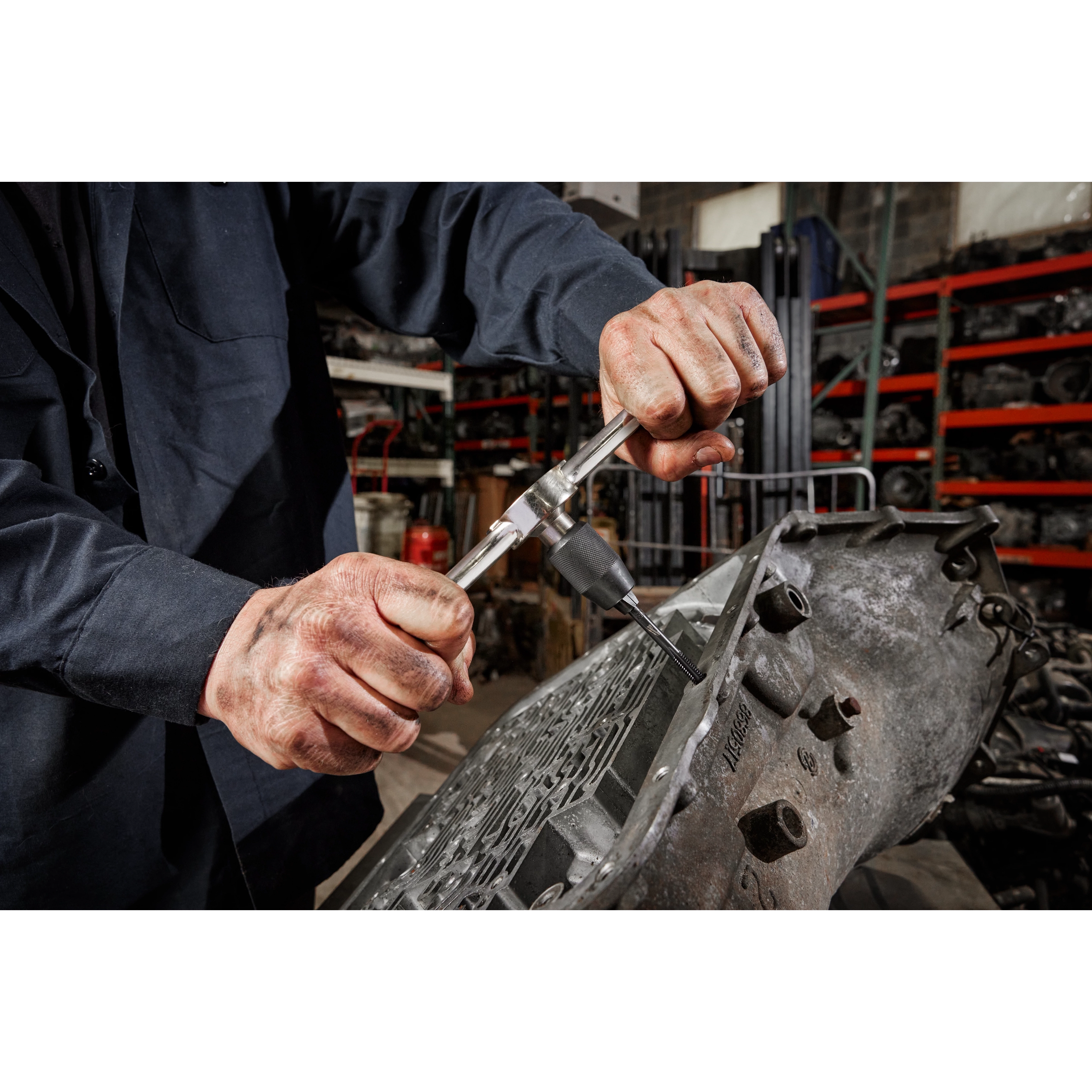 A person uses the Hex-LOK™ 2-in-1 Tap and Die Threading Handle & Tap Collet to work on a metal part in an industrial setting, surrounded by machinery and tools.