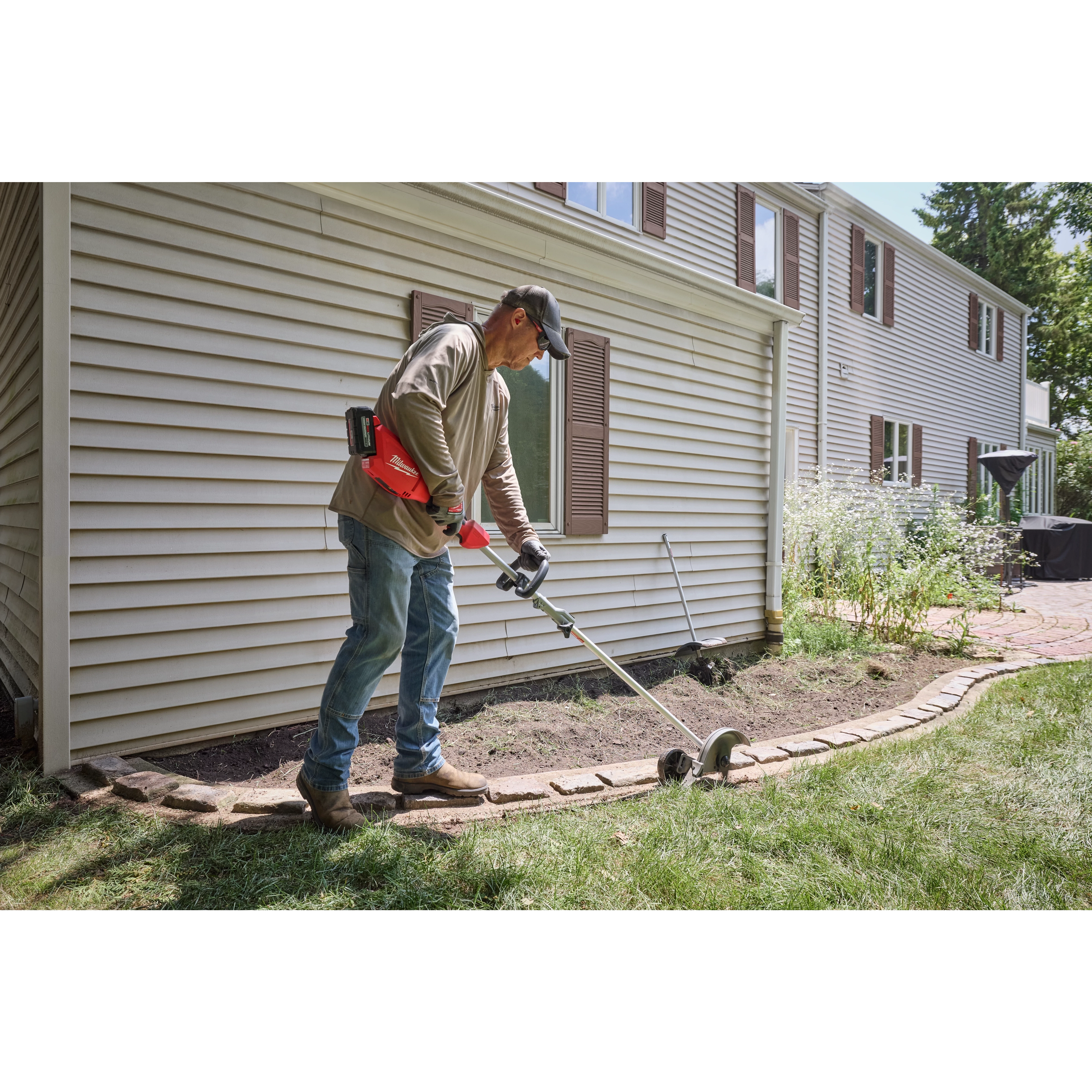 Person edging a lawn with an M18 QUIK-LOK Brushless Power Head beside a house and garden bed.