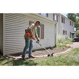 Person edging a lawn with an M18 QUIK-LOK Brushless Power Head beside a house and garden bed.