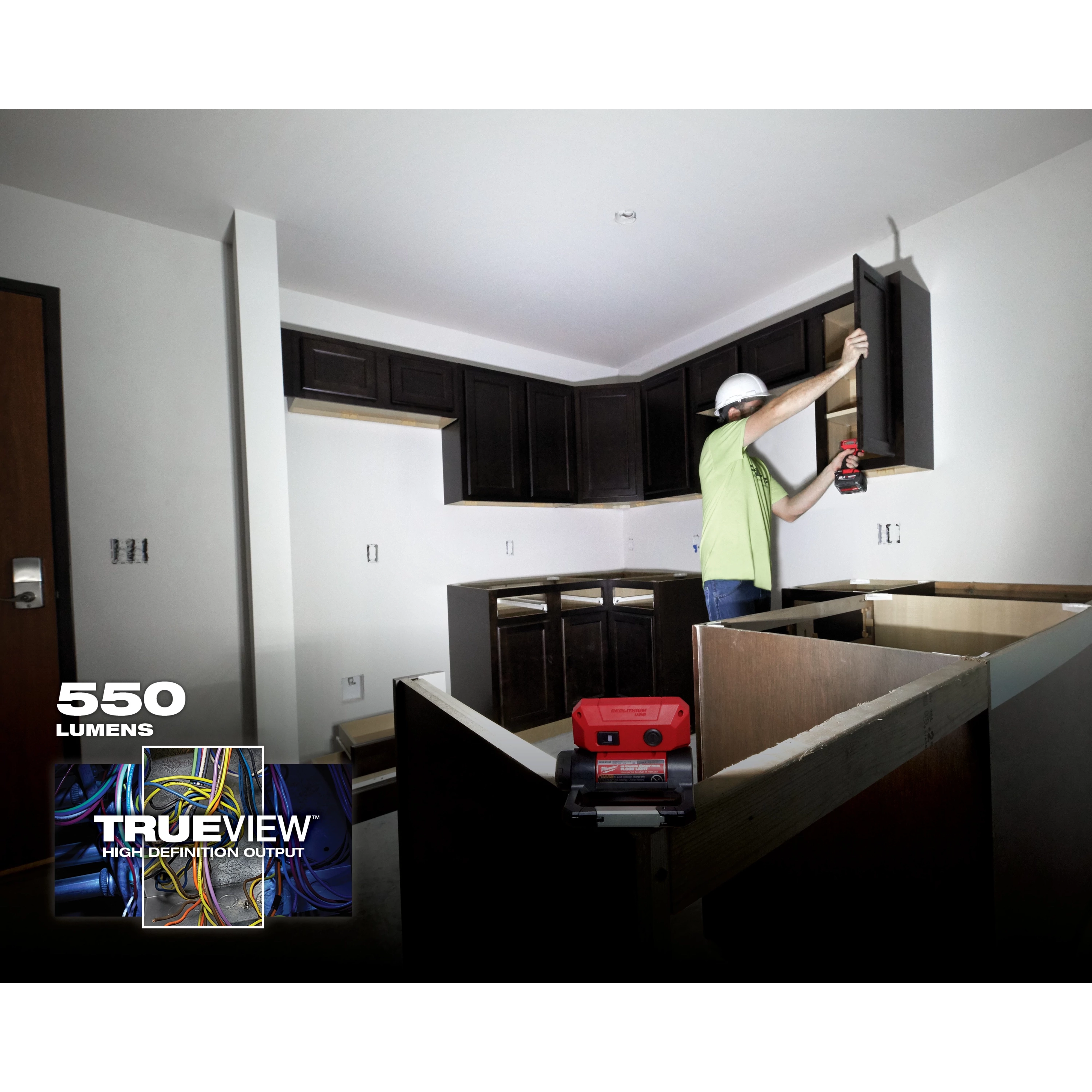 A person using a REDLITHIUM USB ROVER Pivoting Flood Light to illuminate a partially constructed kitchen with dark wood cabinets.