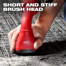 A person uses the red AIR-TIP™ Swiveling Palm Brush on a carpet. The brush features a short and stiff brush head, as noted in the text overlay. The brand logo and product name, Milwaukee AIR-TIP™, are visible on the brush.