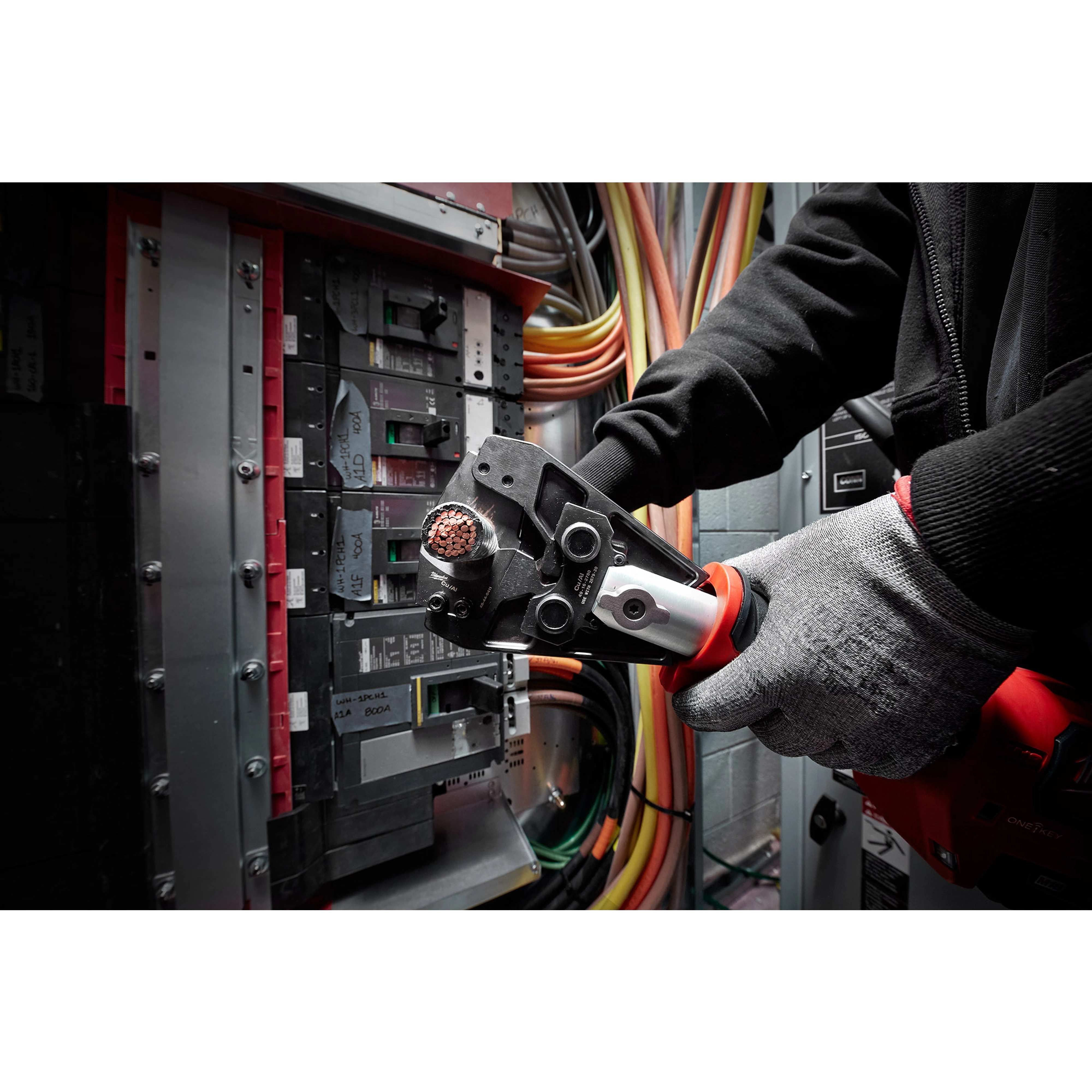 Person using the 750 MCM Cu/Al Cutting Jaw tool to cut a copper wire inside an electrical panel, with colorful cables in the background.