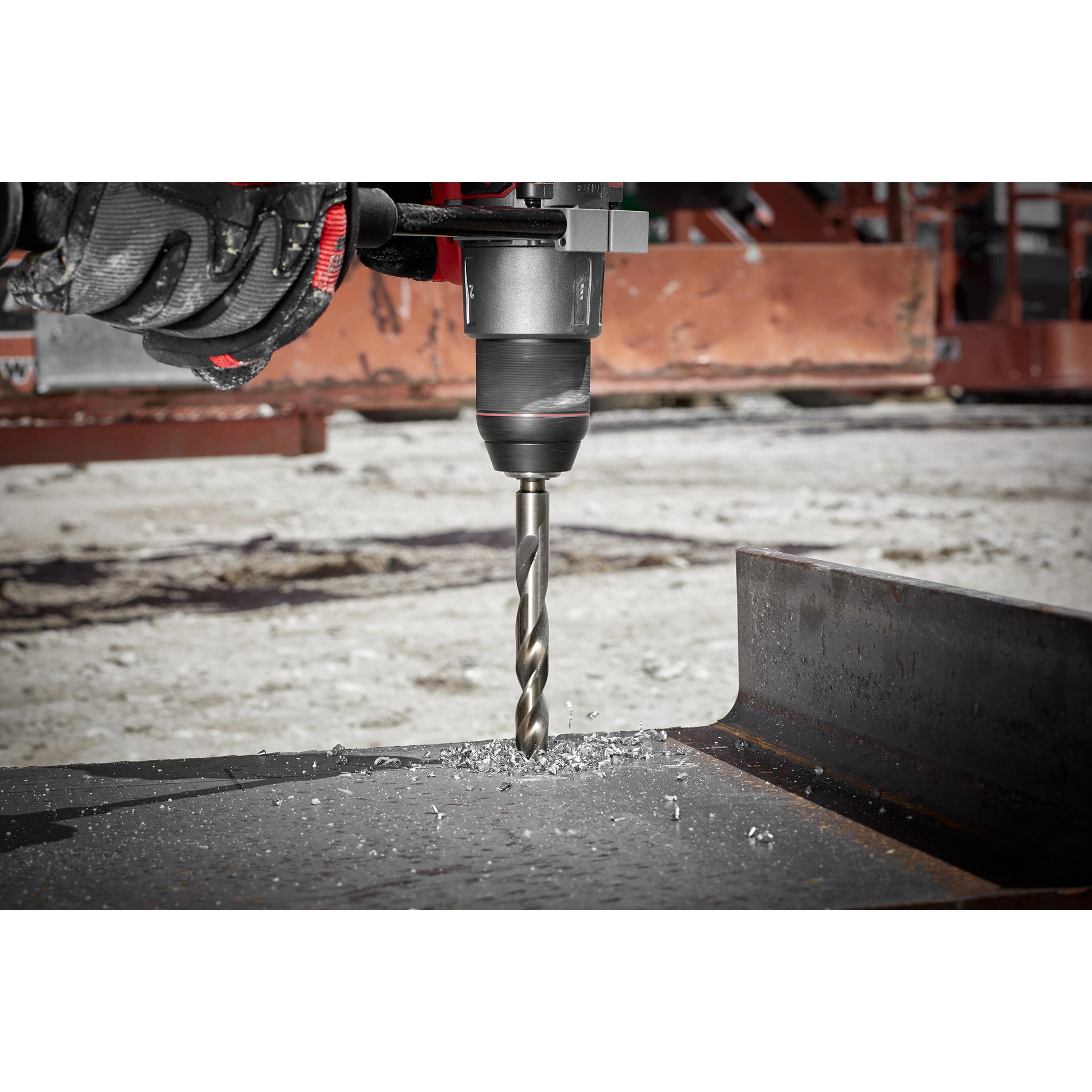 The RED HELIX™ Cobalt 1/2" Drill Bit is shown being used with a power drill to cut through a piece of metal, creating metal shavings. The background displays an industrial work environment.