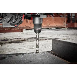 The RED HELIX™ Cobalt 1/2" Drill Bit is shown being used with a power drill to cut through a piece of metal, creating metal shavings. The background displays an industrial work environment.