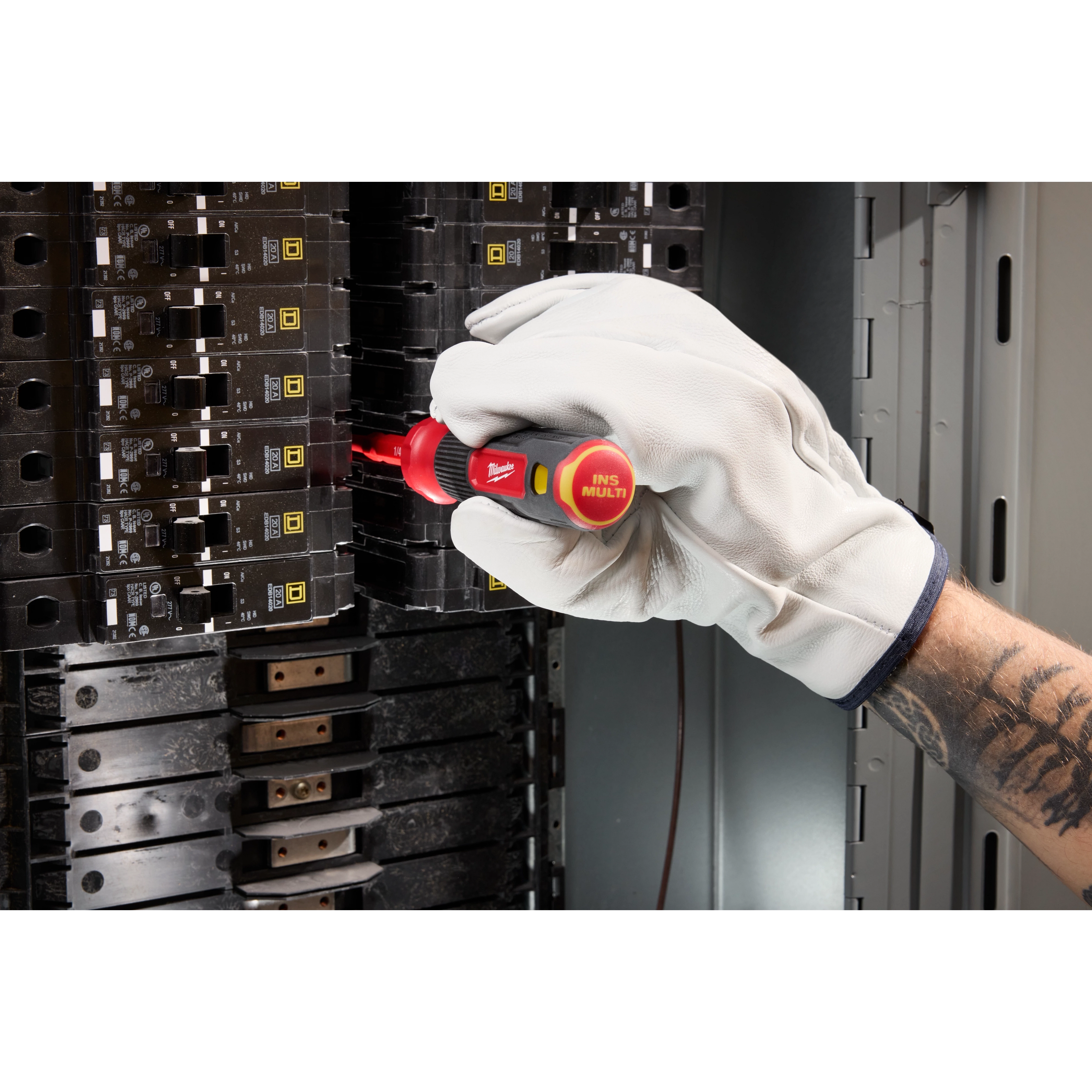A gloved hand uses the 2-in-1 1000V Insulated Flip Shank Multi-Bit Screwdriver to adjust a switch inside an electrical panel.