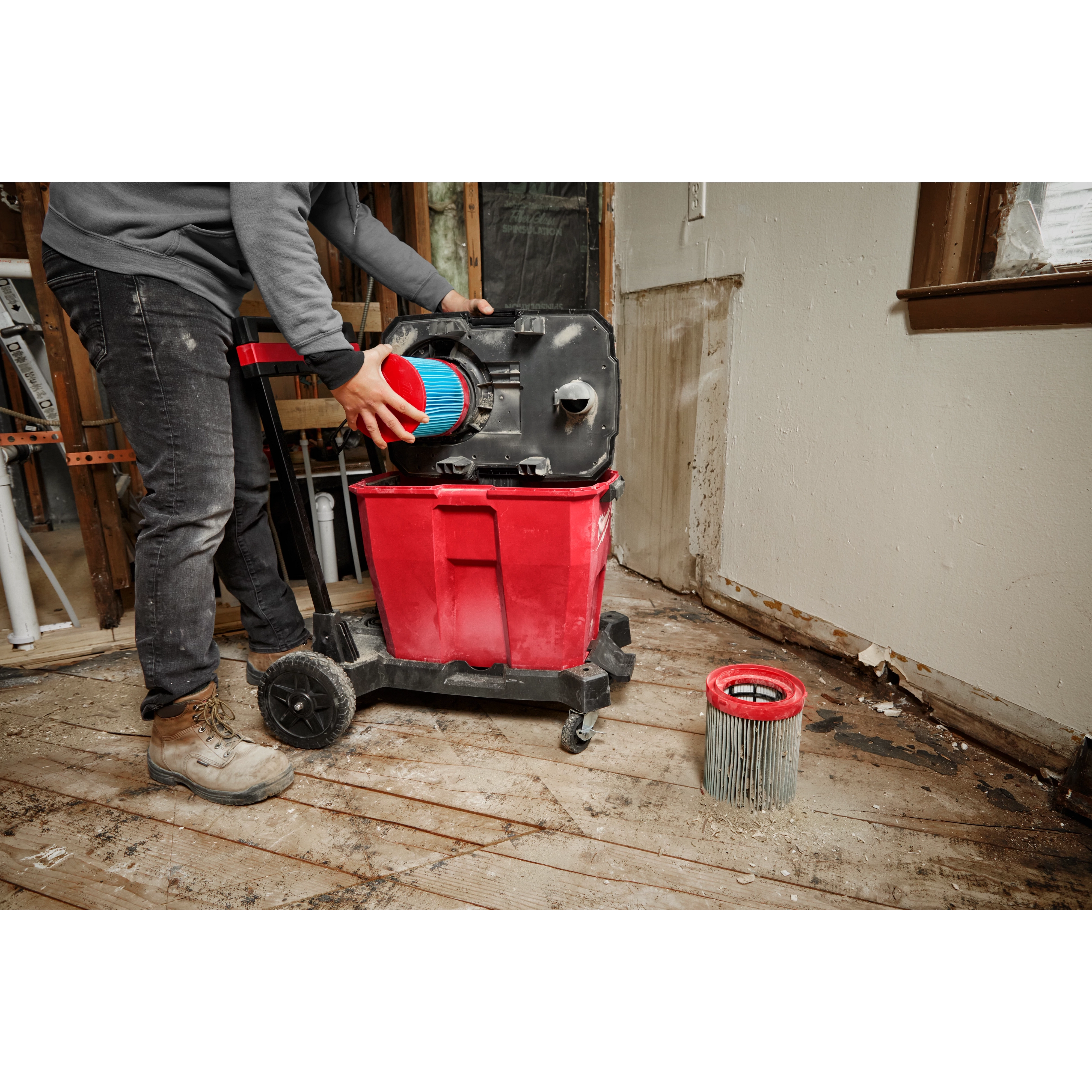 Person replacing the filter in a red Large Wet/Dry Vacuum High Efficiency Filter on a construction site with wooden floors.