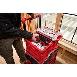 A man using the Divider for PACKOUT Crate to organize red power tools and accessories in a red stacking toolbox on a construction site.