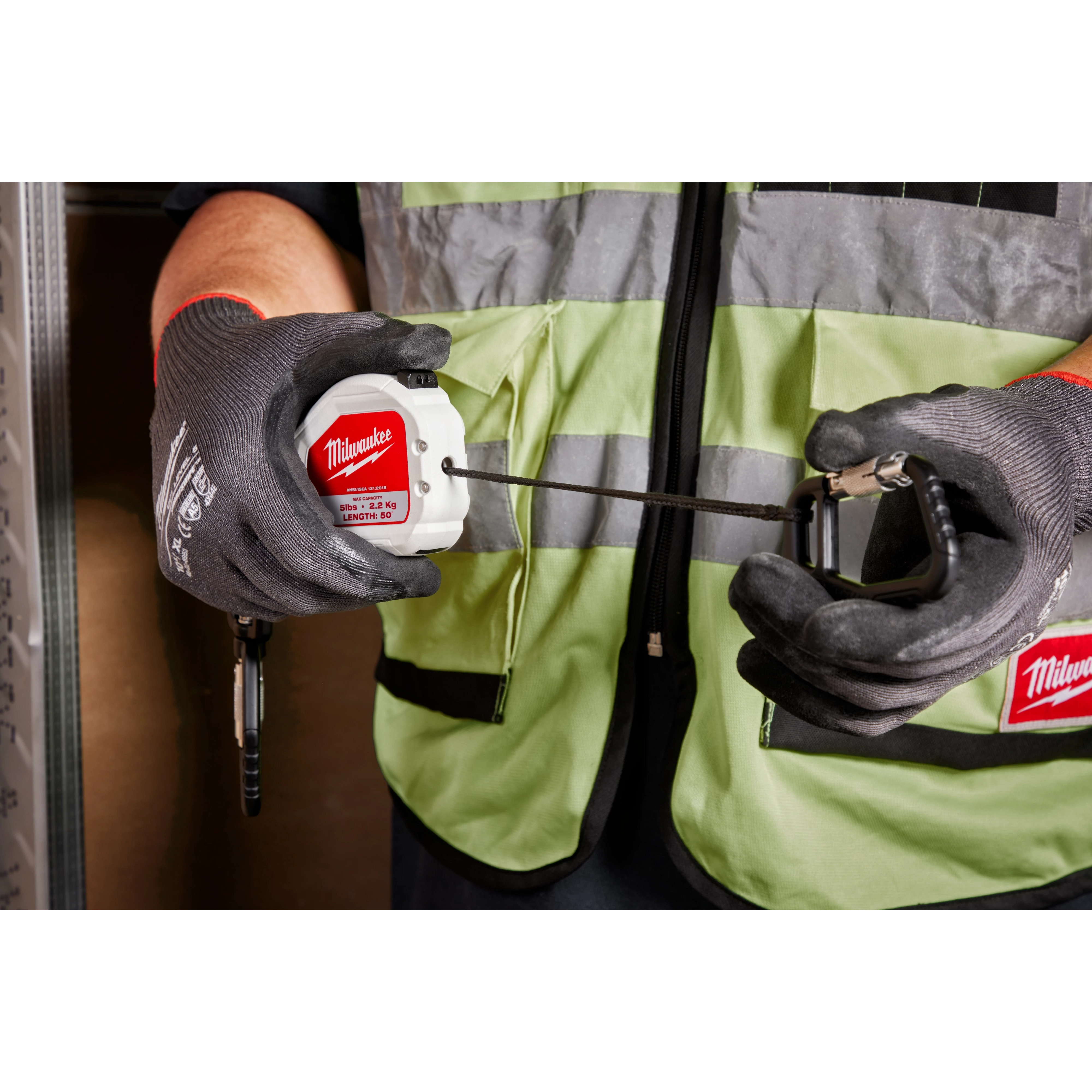 5LB Quick-Connect Retractable Tool Lanyard is being held by a person wearing a safety vest and gloves. The lanyard is extended and features a carabiner clip. The product is maximum load rated for 5 pounds and designed to prevent tool drops, ensuring safety on work sites.