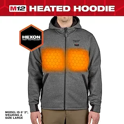 The M12™ Heated Hoodie features Hexon Heat Technology with visible heating elements on the chest area. It is gray, has a front zipper, and includes pockets. The model is 6'2", wearing a size large.