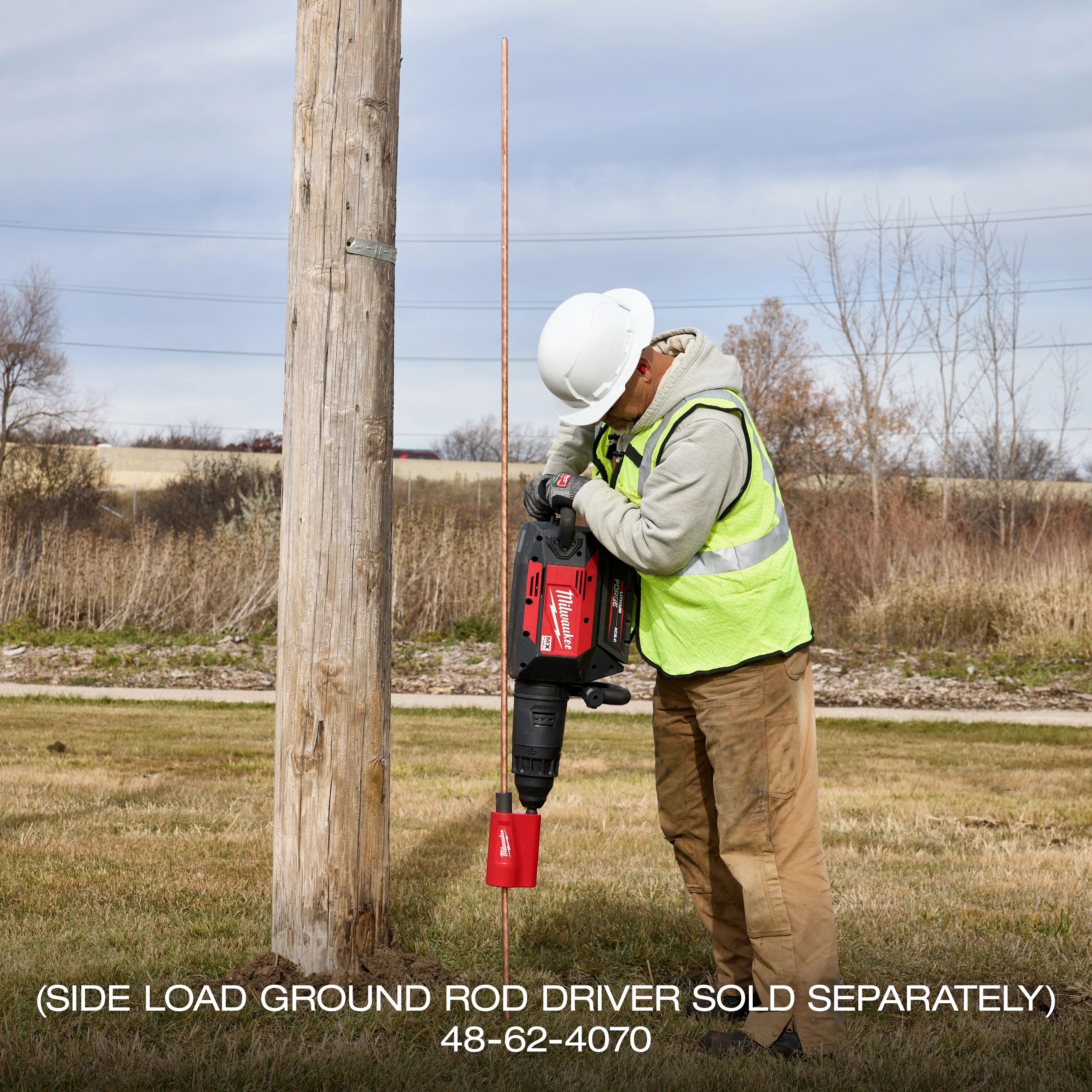 Worker using MX FUEL 27 lb SDS MAX Demolition Hammer to drive a ground rod beside a utility pole outdoors.