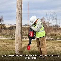 Worker using MX FUEL 27 lb SDS MAX Demolition Hammer to drive a ground rod beside a utility pole outdoors.