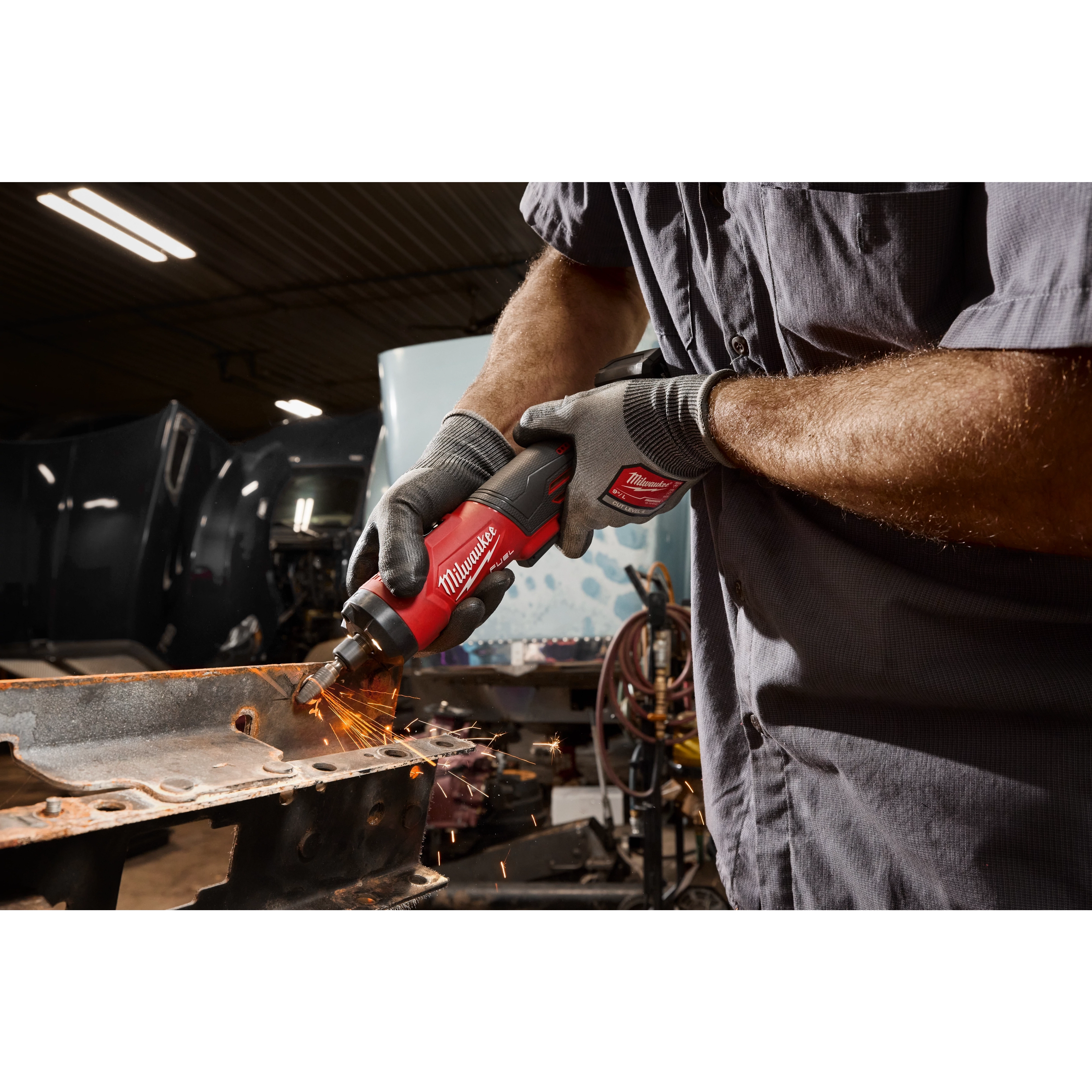 Gloved hands using an M12 FUEL 1/4" Straight Die Grinder to grind metal, creating visible sparks.