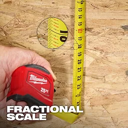 Hand holding a 25ft Tape Measure with extended yellow blade showing fractional scale on a wood surface.