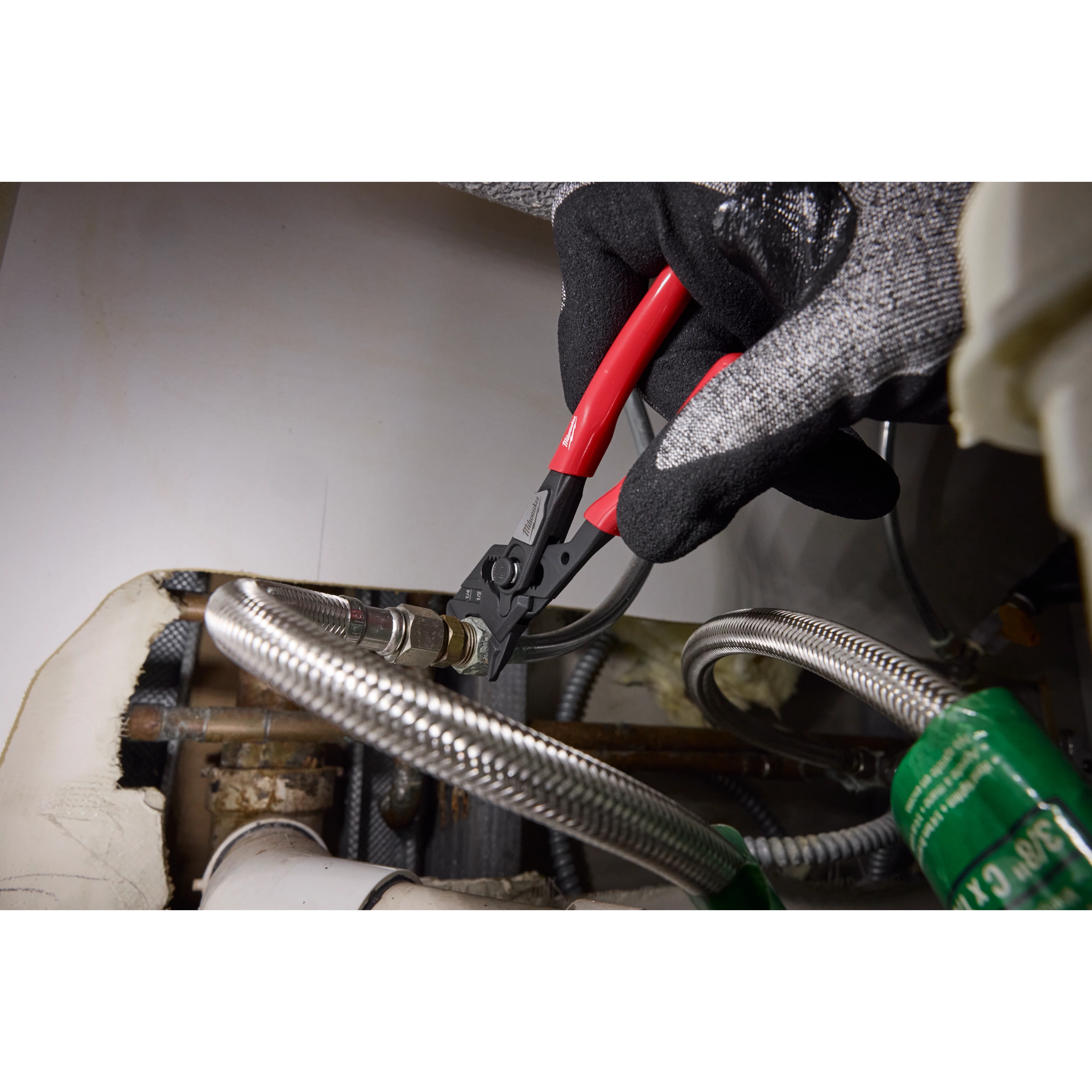 A gloved hand holds the 5" Pliers Wrench, gripping and adjusting a metallic hose connector in what appears to be an industrial or workshop setting. The tool features a red handle and is in use, demonstrating its function.