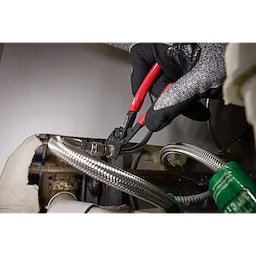 A gloved hand holds the 5" Pliers Wrench, gripping and adjusting a metallic hose connector in what appears to be an industrial or workshop setting. The tool features a red handle and is in use, demonstrating its function.