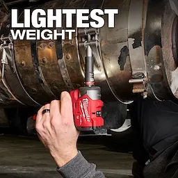 A person uses a Milwaukee M12 FUEL™ 3/8" Subcompact Impact Wrench with Friction Ring on a large metal pipe with text "LIGHTEST WEIGHT" above.