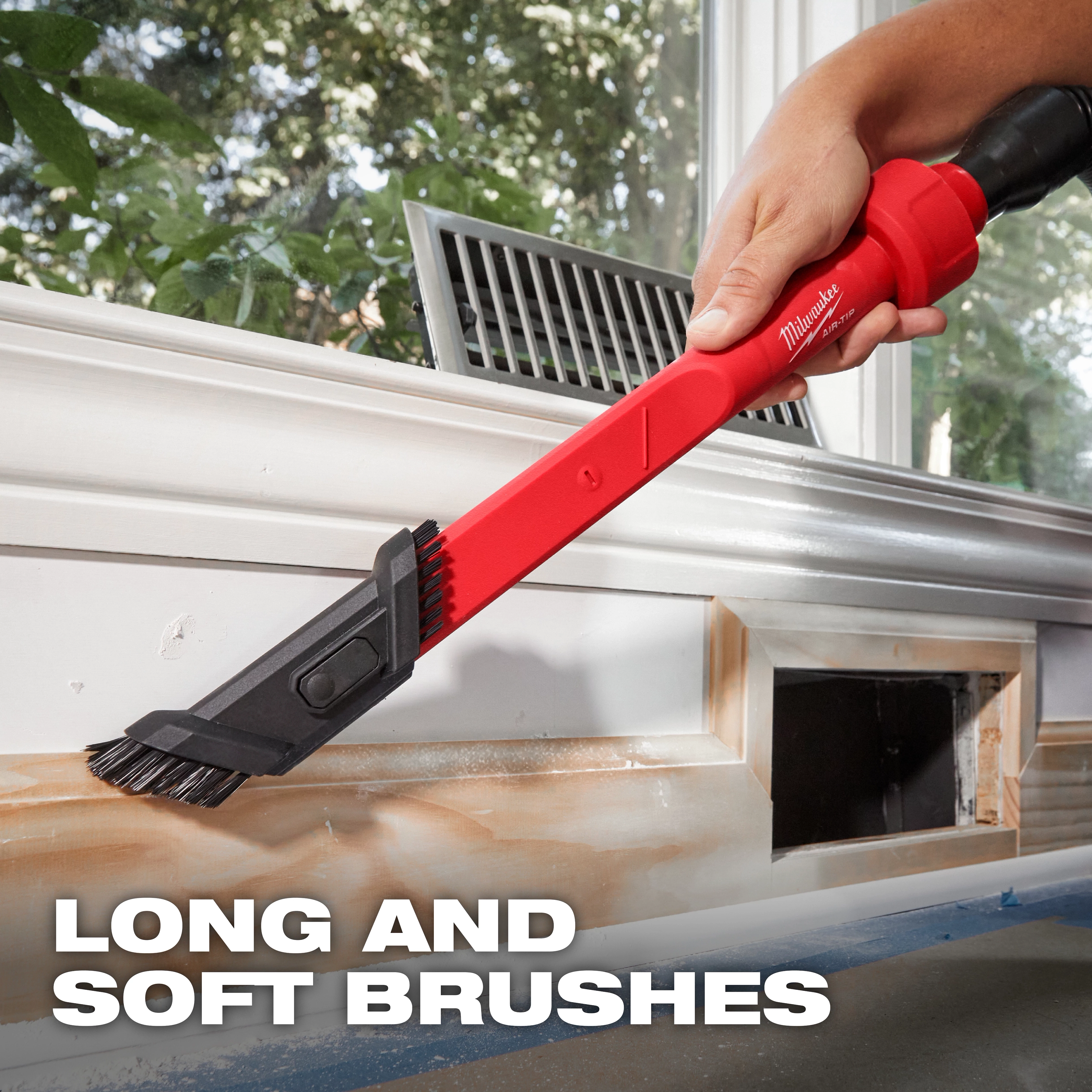 A person using the AIR-TIP™ 3-in-1 Crevice and Brush Tool to clean a window frame. The tool has long and soft brushes. The background shows greenery outside the window. Caption at the bottom says "LONG AND SOFT BRUSHES".