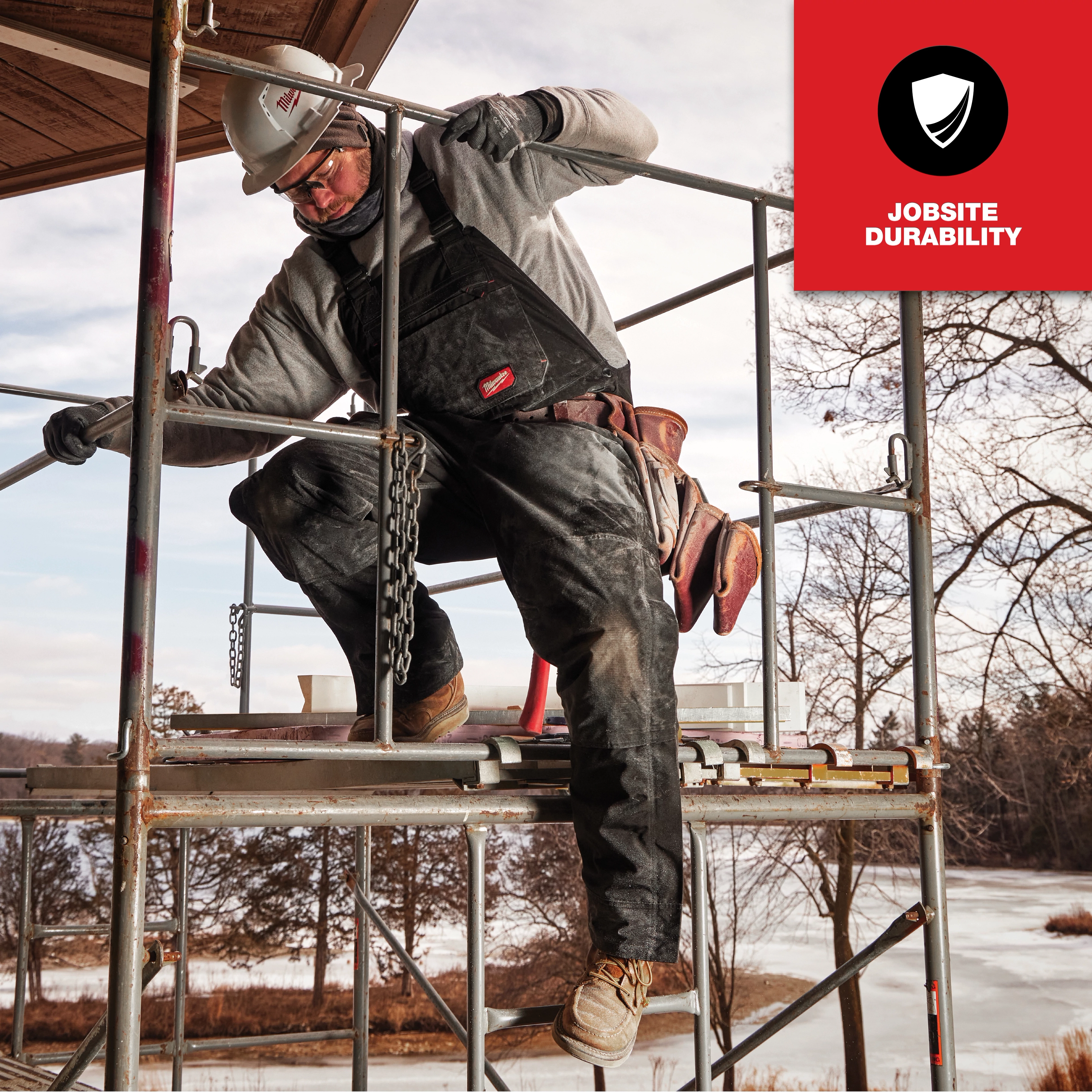 Worker wearing FREEFLEX Insulated Bib Overalls, standing on scaffolding at a construction site. Red badge reads "Jobsite Durability."
