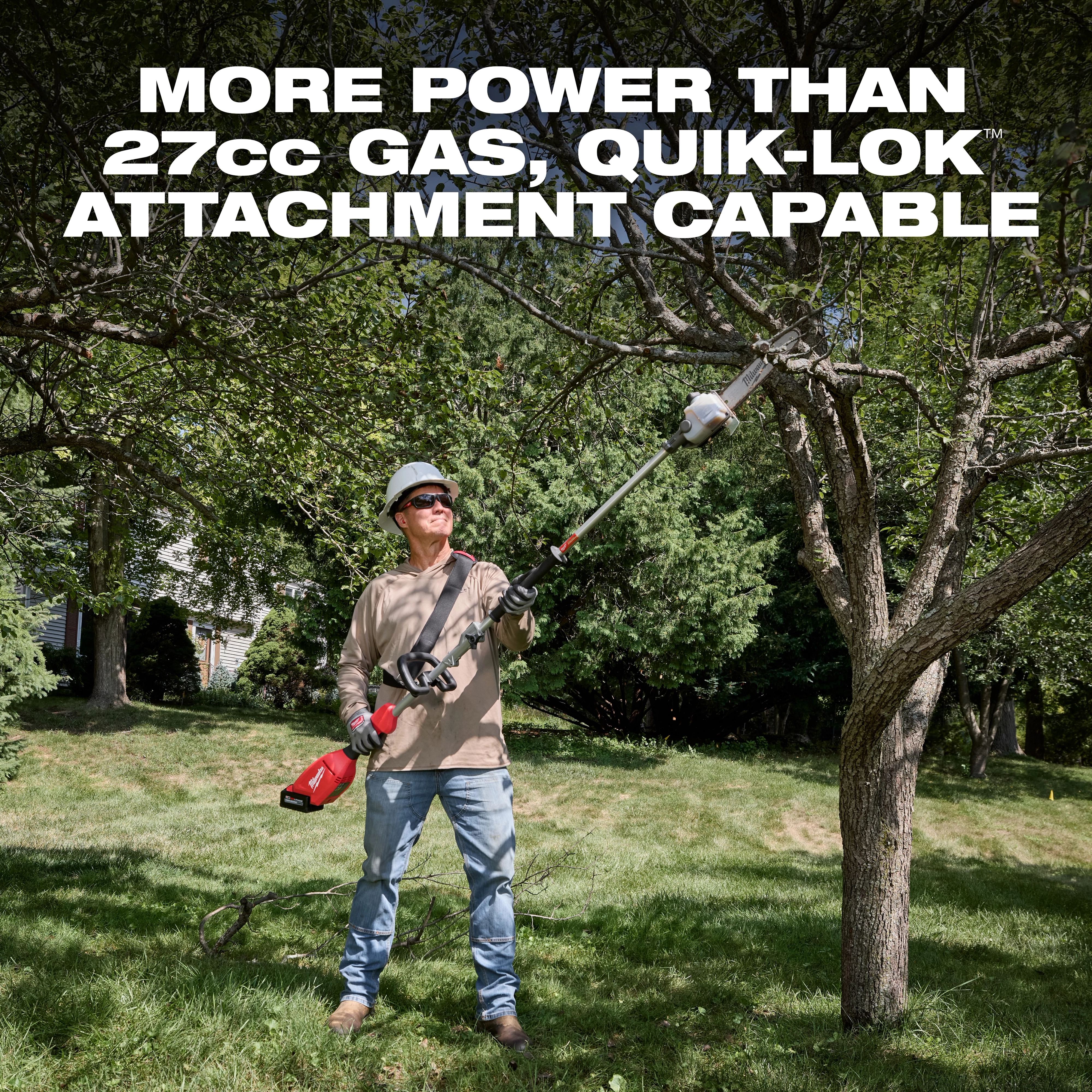 Worker using an M18 QUIK-LOK Brushless Pole Saw to trim branches on a tree in a grassy yard.