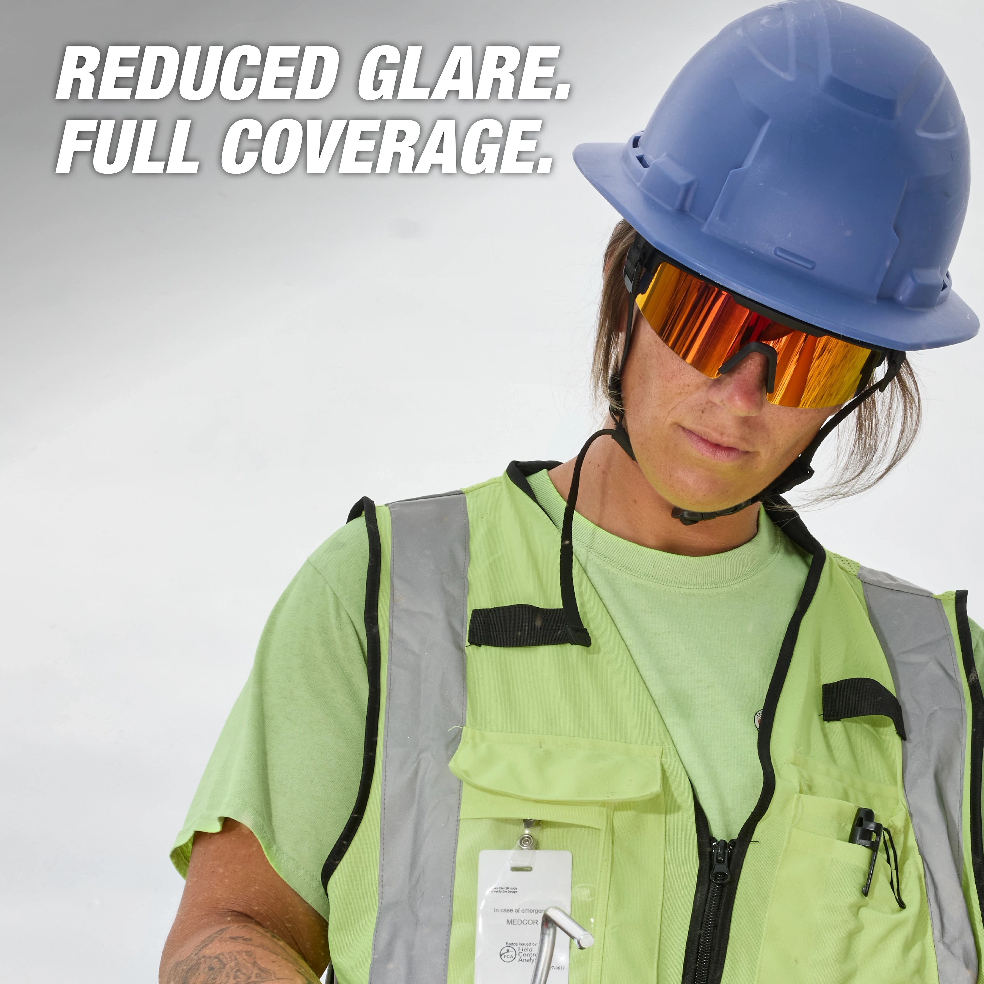 A person in a green safety vest and blue hard hat wears Polarized Wrap Around Safety Glasses - Red Mirrored Dual Coat Lens. Text reads "Reduced Glare. Full Coverage."