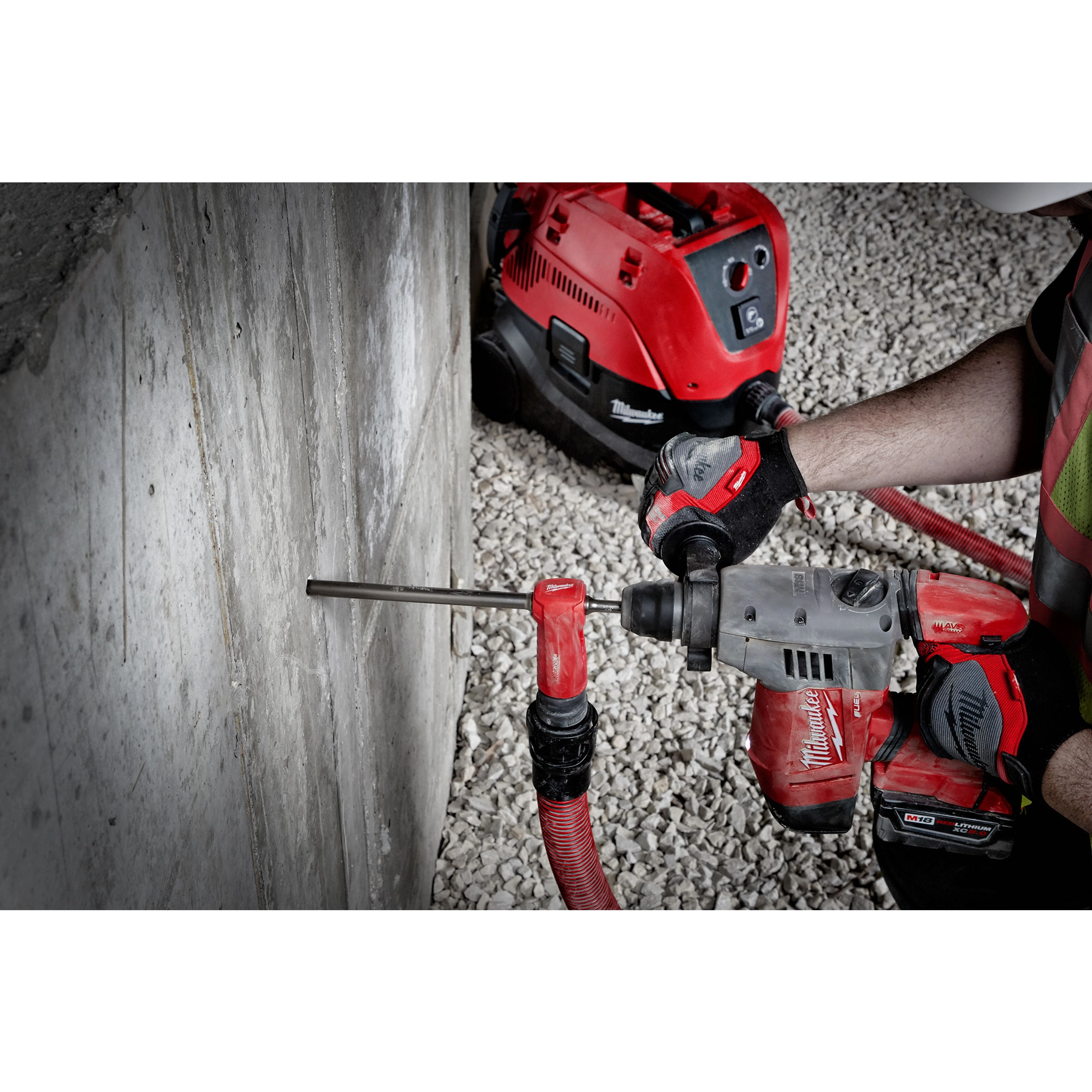 SDS%20Vacuum%20Bit in use with a power drill, drilling into a concrete wall, connected to a red vacuum system on gravel ground.