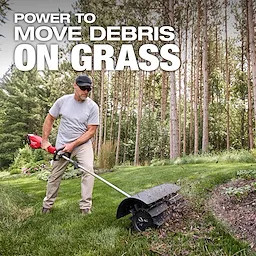 Person using an M18 FUEL QUIK-LOK Rubber Broom Attachment to clear debris from grass near a wooded area.
