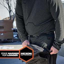 Person wearing Milwaukee Heated Merino Wool Baselayer Pants outdoors, adjusting outer pants in a snowy setting.