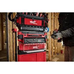 The PACKOUT Tool Box Magnetic Bin Attachment is shown connected to a stack of red and black Milwaukee PACKOUT toolboxes in a workshop.