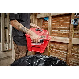 A person empties debris from a Milwaukee 6 Gallon Wet/Dry Vacuum Tank into a black garbage bag at a construction site.