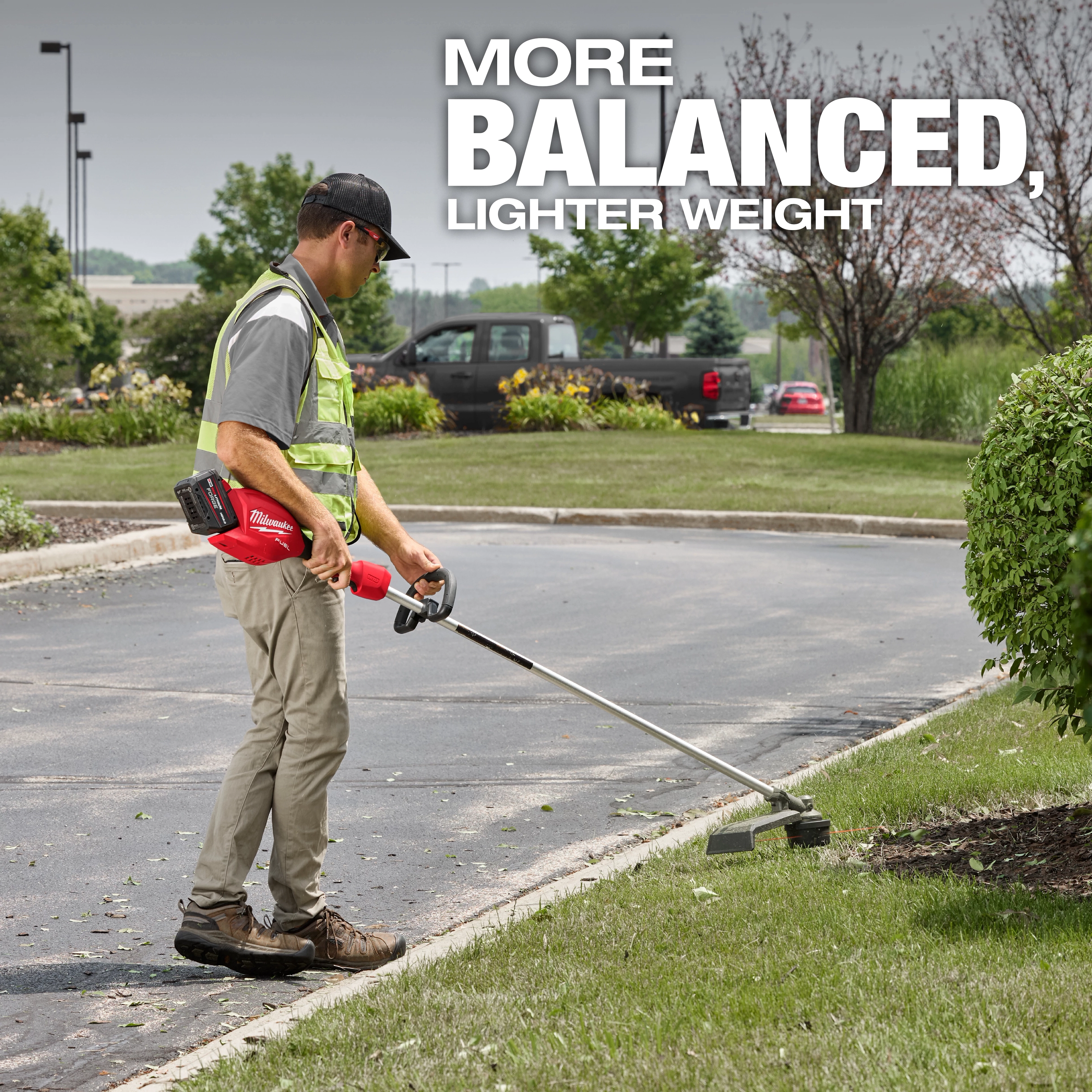 A person uses a red cordless string trimmer on a grassy lawn beside a paved path. Text reads "MORE BALANCED, LIGHTER WEIGHT."