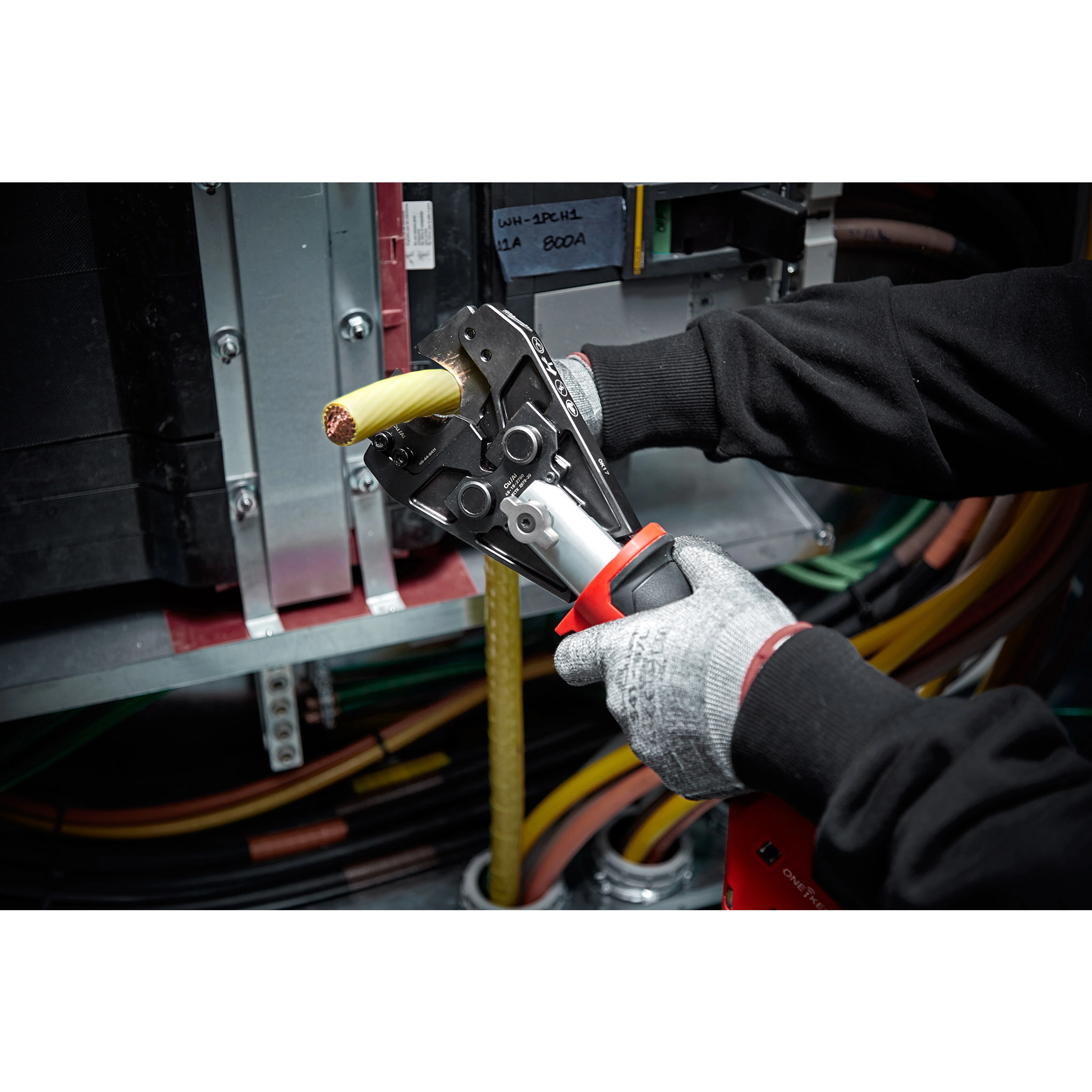 A person uses the 750%20MCM%20Cu%2FAl%20Cutting%20Jaw to cut a thick yellow electric cable inside an industrial setting.