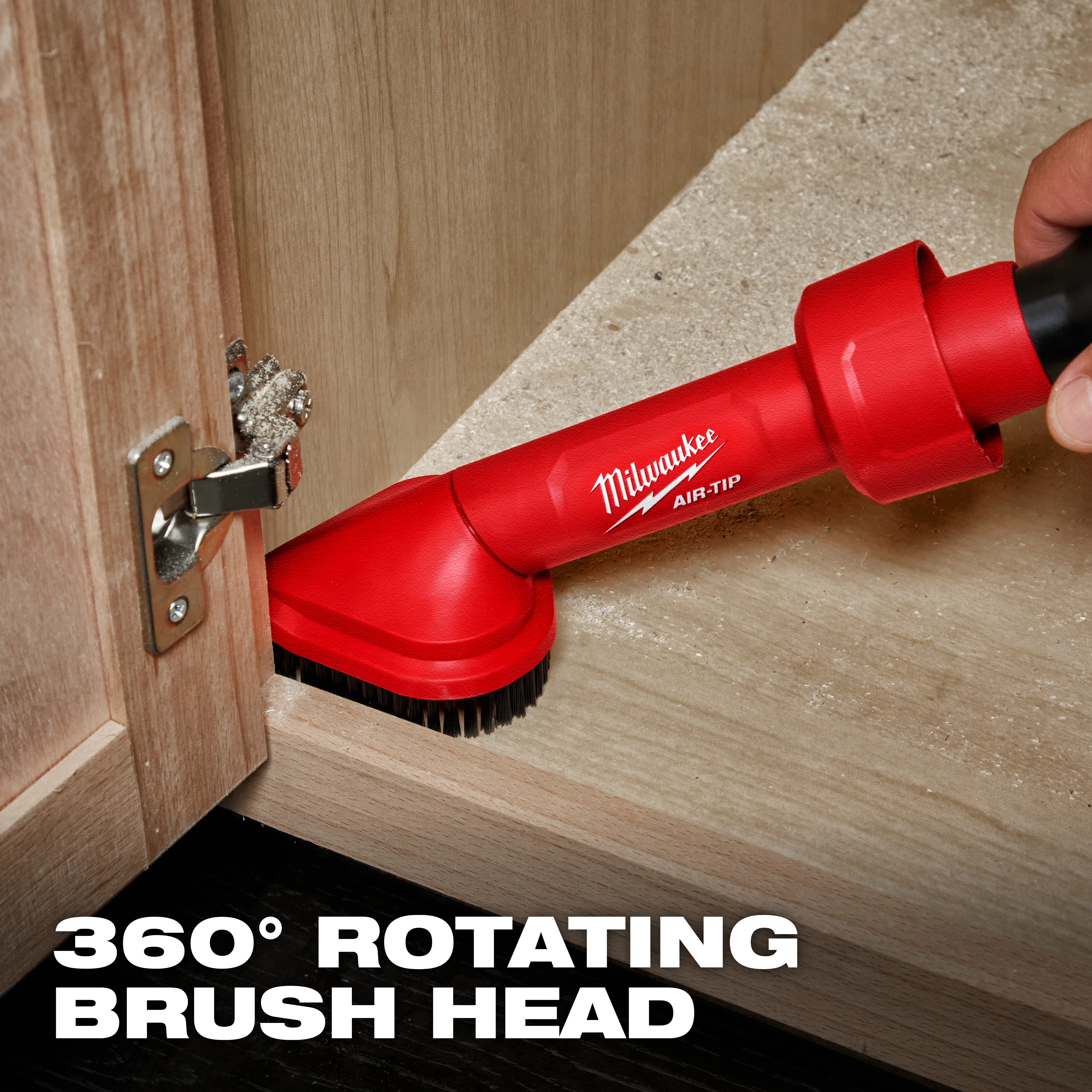 The image shows an AIR-TIP™ Rotating Corner Brush Tool by Milwaukee being used inside a wooden cabinet. The red tool with a 360° rotating brush head is designed for cleaning corners and hard-to-reach areas. There is text at the bottom saying "360° Rotating Brush Head."