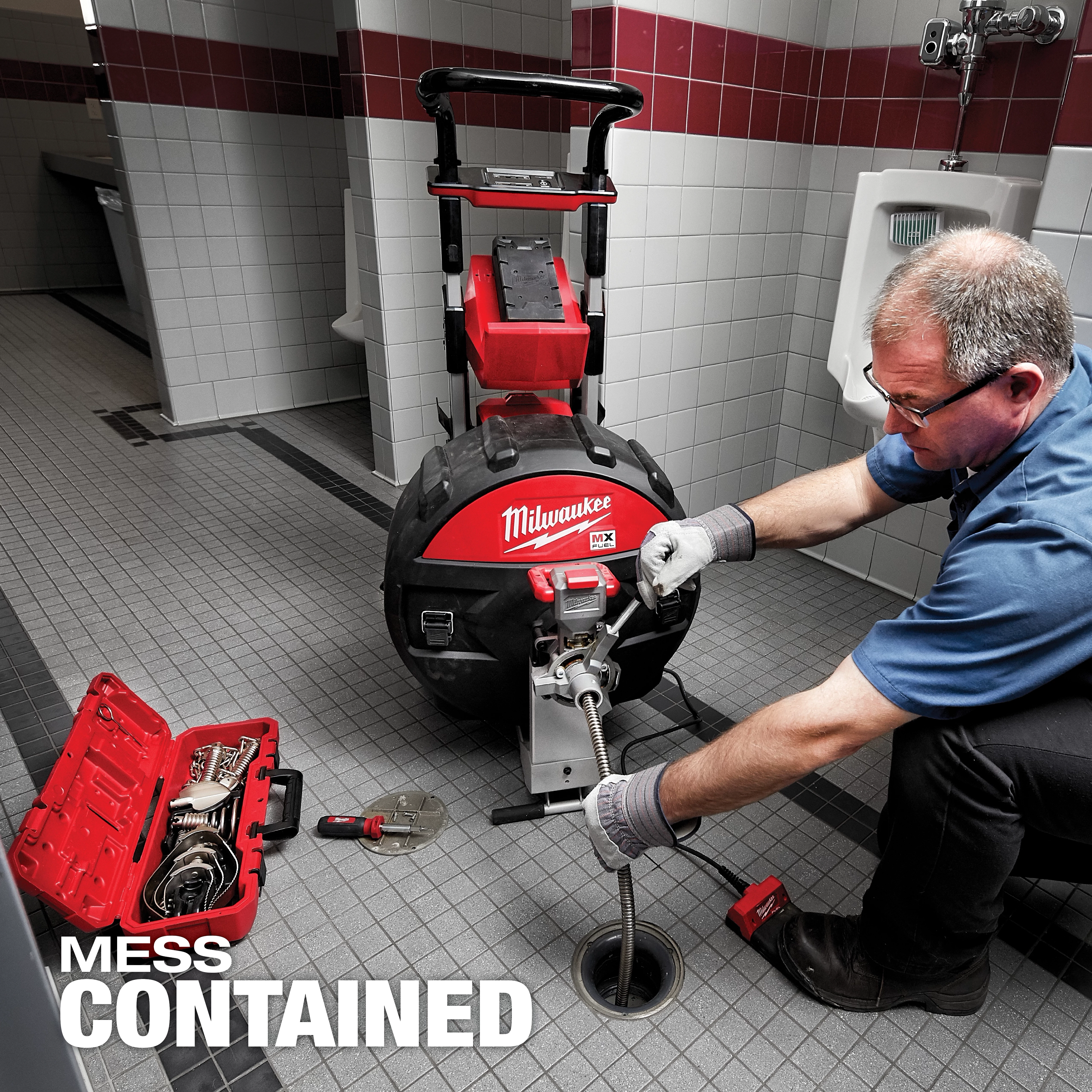 A worker operates the MX FUEL Sewer Drum Machine w/ POWERTREDZ in a tiled restroom, with a tool case open beside him.