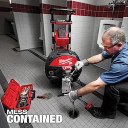 A worker operates the MX FUEL Sewer Drum Machine w/ POWERTREDZ in a tiled restroom, with a tool case open beside him.