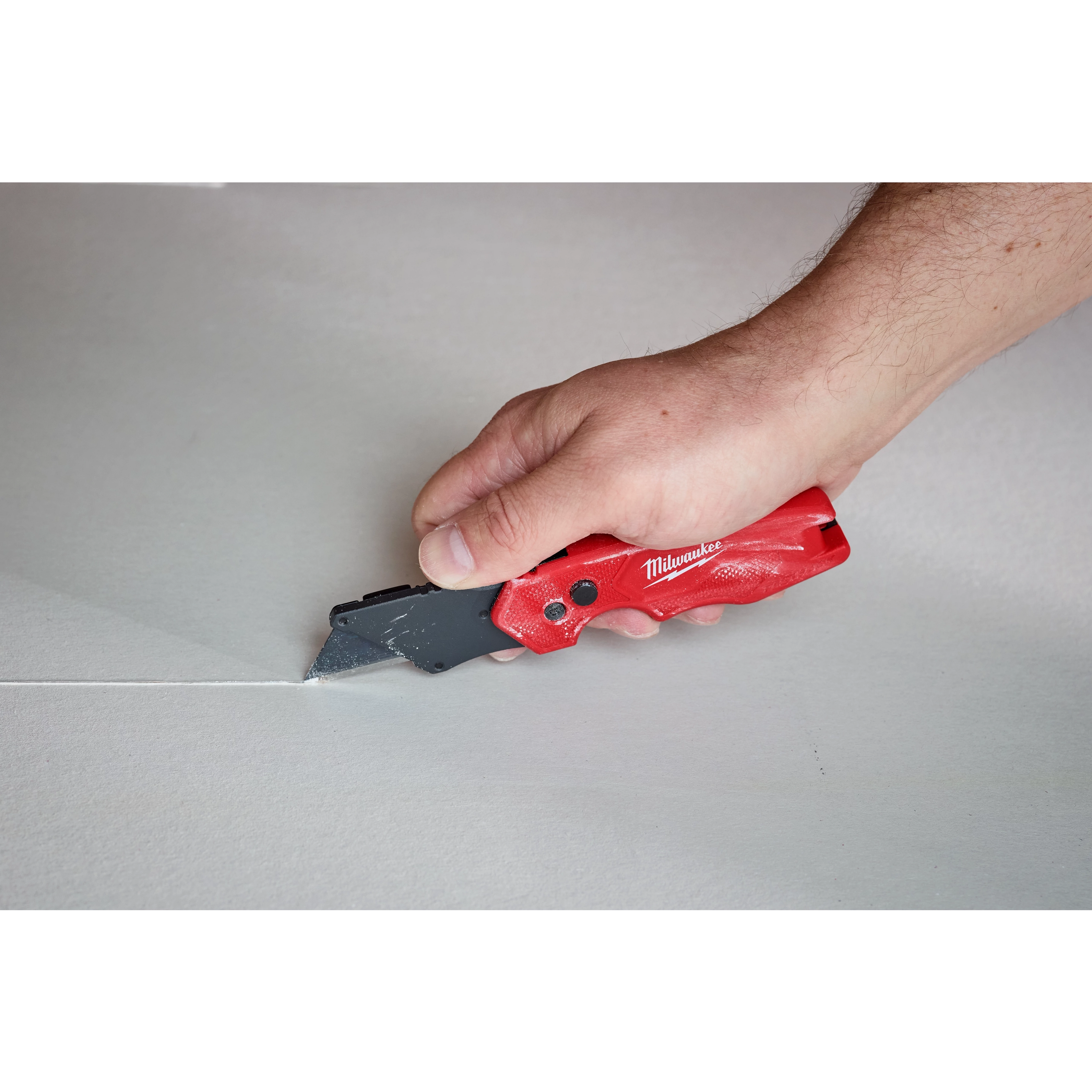 Hand using a FASTBACK Compact Folding Utility Knife to cut a straight line on a flat surface.