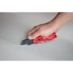 Hand using a FASTBACK Compact Folding Utility Knife to cut a straight line on a flat surface.